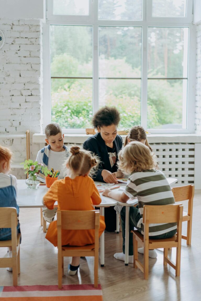 A teacher guides children around a table in a bright, engaging classroom setting.